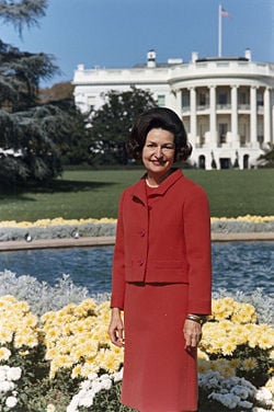 Lady Bird Johnson, photo portrait, standing at rear of White House, color.jpg